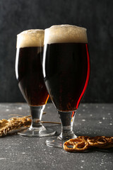 Glasses of cold dark beer with pretzels and wheat on grunge table against black background