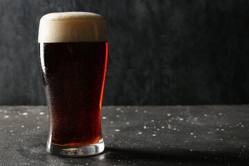 Glass of cold dark beer on grunge table against black background