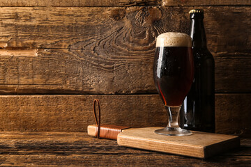 Glass and bottle of cold dark beer on table against wooden background