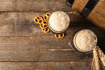 Glasses and barrel of cold dark beer with wheat and pretzels on wooden background