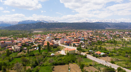 Fototapeta na wymiar Scenic spring view from drone of Yesildag village with residential houses and mosque in green valley surrounded by mountains with peaks covered with snow, Turkey