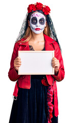 Woman wearing day of the dead costume holding empty white chalkboard thinking attitude and sober expression looking self confident