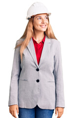 Beautiful young woman wearing architect hardhat looking away to side with smile on face, natural expression. laughing confident.