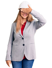 Beautiful young woman wearing architect hardhat smiling and laughing with hand on face covering eyes for surprise. blind concept.