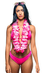 Beautiful hispanic woman wearing bikini and hawaiian lei skeptic and nervous, frowning upset...