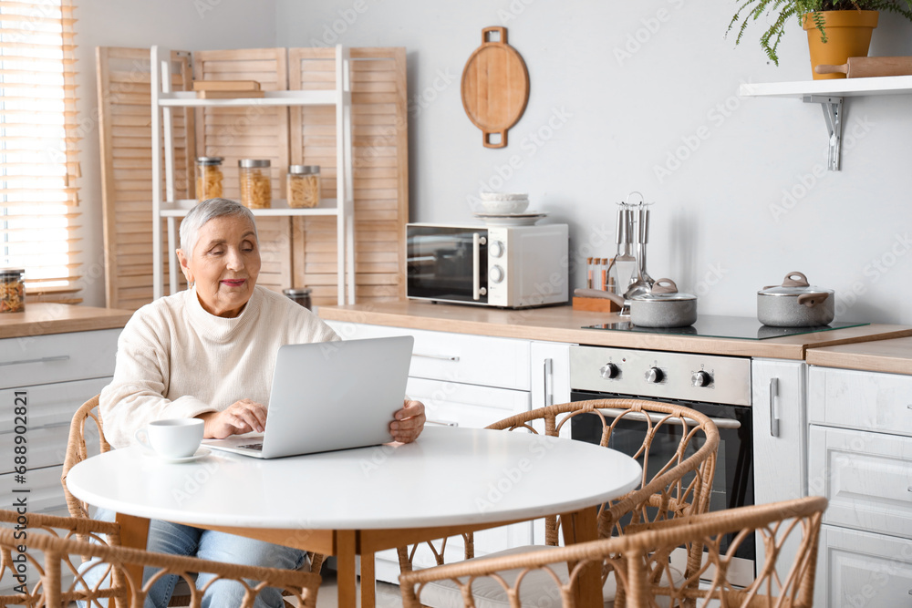 Canvas Prints Senior woman using laptop at table in kitchen