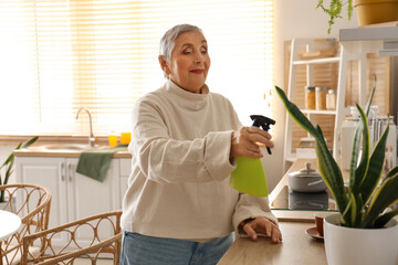 Senior woman watering plant in kitchen