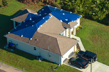 Aerial view of damaged in hurricane Ian house roof covered with blue protective tarp against rain...