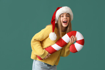 Happy young woman in Santa hat with candy cane pillow on green background