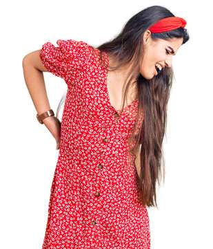 Brunette teenager girl wearing summer dress suffering of backache, touching back with hand, muscular pain