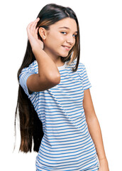 Fototapeta premium Young brunette girl with long hair wearing casual striped t shirt smiling with hand over ear listening and hearing to rumor or gossip. deafness concept.