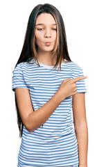 Fototapeta premium Young brunette girl with long hair pointing with fingers to the side making fish face with mouth and squinting eyes, crazy and comical.