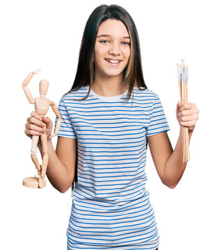 Young brunette girl with long hair holding small wooden manikin and pencils smiling and laughing hard out loud because funny crazy joke.