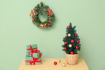 Shelving unit with Christmas tree in pot and gifts near green wall