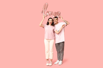Loving young couple with balloon in shape of word LOVE on pink background. Celebration of Saint Valentine's Day
