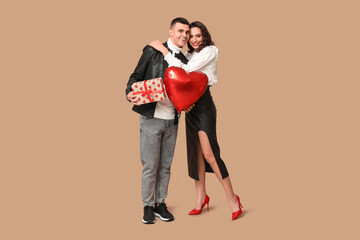 Loving young couple with heart-shaped balloon and gift box on brown background. Celebration of...