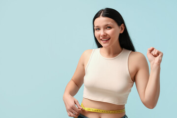 Beautiful young happy woman with measuring tape on blue background. Weight loss concept