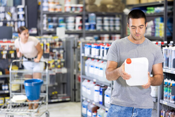 Man examines plastic canister buys, collects necessary supplies in store according to list for apartment renovation. Repair and construction items, paint and varnish products, accessories, supermarket