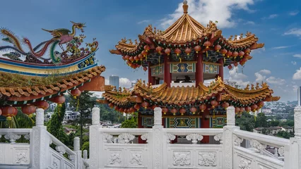 Foto op Plexiglas The beautiful tower of a Chinese Thean Hou Temple against a blue sky and clouds. Elegantly curved roof, bright lanterns, carved decorations. In the foreground there is a white stone railing. Malaysia. © Вера 