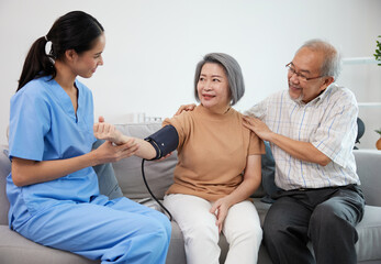 caregiver or nurse measure blood pressure to senior woman on sofa