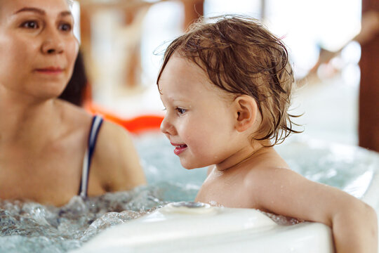 Cheerful woman with little child swim together in whirlpool bath. Happy mother and baby enjoy bathing in water with swirling bubbles at aquapark