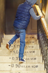 Boy wearing jeans and vest goes upstairs with burnt calories marks on steps. Kid runs up steps to apartment. Playing child - obrazy, fototapety, plakaty