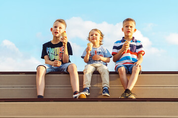 Little boys brothers eats tasty chocolate ice cream sitting on wooden bench watching movie on huge screen against sky with clouds in park - 688918816