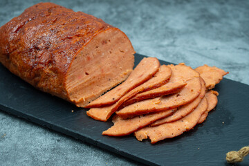 Vegan meat alternative- seitan  made with gluten and tofu, seasoned with spices, glazed with BBQ sauce. White plate, sliced, slate board