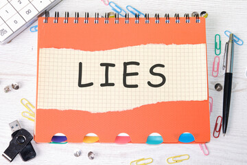 Lies word is written on a sheet in a cage lying on a notebook on the table next to stationery - obrazy, fototapety, plakaty