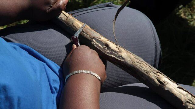 Boyscouts woman leader carves a walking stick with a knife for hiking