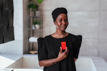 Confident African girl in Black turban and traditional black clothes holds credit card looks at...