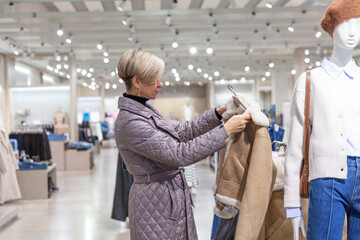 A woman chooses a warm jacket in a store. Seasonal change of collection. Style, fashion and beauty.