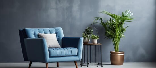 Real photograph of a blue armchair in a living room with a sofa, table, posters, and a plant on a pouf.