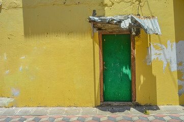 a green wooden door with yellow walls showing some of the peeling paint on the old house