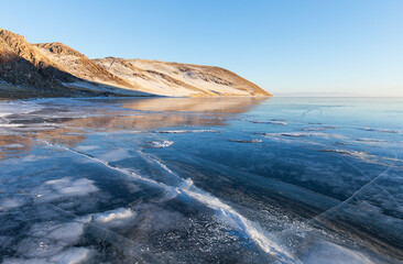 Beautiful winter landscape of frozen Baikal Lake in January at sunset. View of snowy coastal hills...