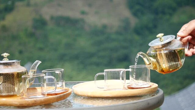 A hand pouring tea from glass teapot on wooden serving tray, hands pouring tea from teapot, Cropped shot of pouring tea in traditional chinese tea ware