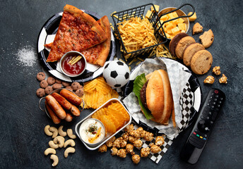 Saturated fats. Football time. TV remote control and snacks - chips, popcorn, cookies, cheese, sauce, fries, burger, nuts