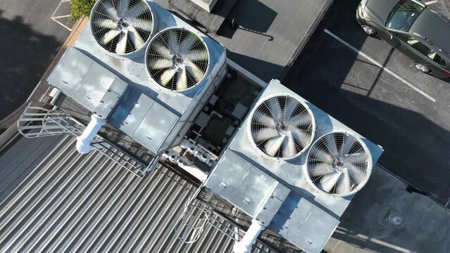 Spinning shot of air conditioning utility unit on roof of industrial building. Top down aerial orbit. Fan rotating as cooling tool.