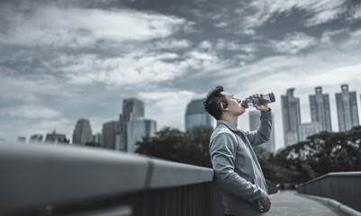 Young sport man drink water after jogging, running in the park. Sport thirsty and resting after...