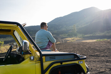 man enjoying beautiful rocky landscapes, sitting on the car hood on the roadside. Traveling on the...
