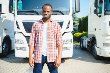 Front view. Young african truck driver is with his vehicle at daytime.
