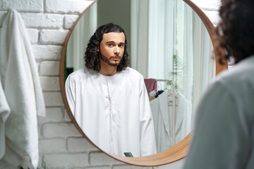 Young Arab man getting ready and looking at the mirror in the bathroom