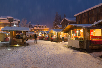 Obraz premium Illuminated stalls in the evening during the Christmas period at a mountain village in the European Alps during a heavy snowfall, Macugnaga, north Italy 