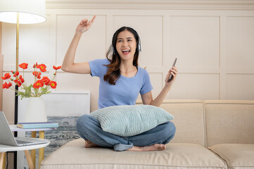 Joyful Asian woman listening to the music and dancing to the song in her living room.