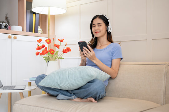 Joyful Asian woman listening to the music and dancing to the song in her living room.