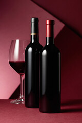 Glass and bottles of red wine on a red background.