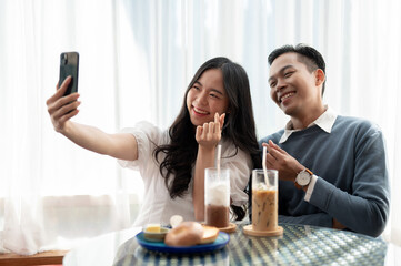 Young Asian couple having a date in a cafe, having good time together and playing with smartphone.