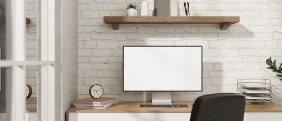 A minimalist white office desk workspace with a computer on a wood table against a white brick wall.
