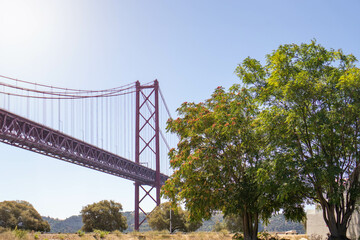 Daytime View of Lisbon Iconic 25 de Abril Bridge: A Horizontal Landscape Shot from Ground Level, Capturing the Majestic Red Suspension Bridge Spanning the Tagus River,