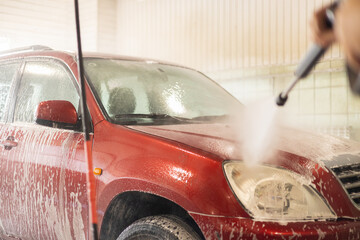 At a self-service car wash, a man washes his red car. The driver brought the car to wash from dirt...